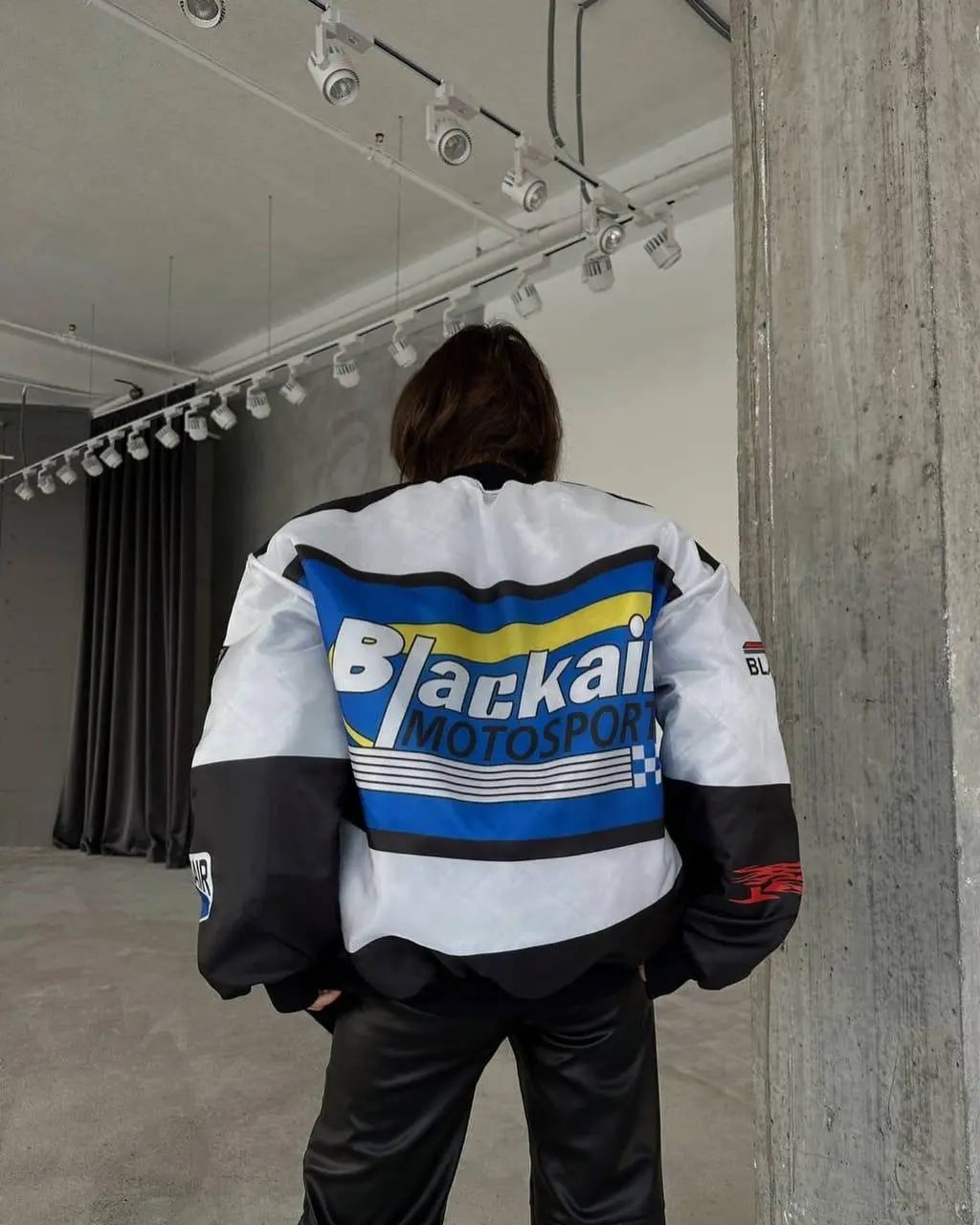 Woman wearing oversized Blackair motorsport jacket with bold blue and yellow graphic, streetwear fashion.