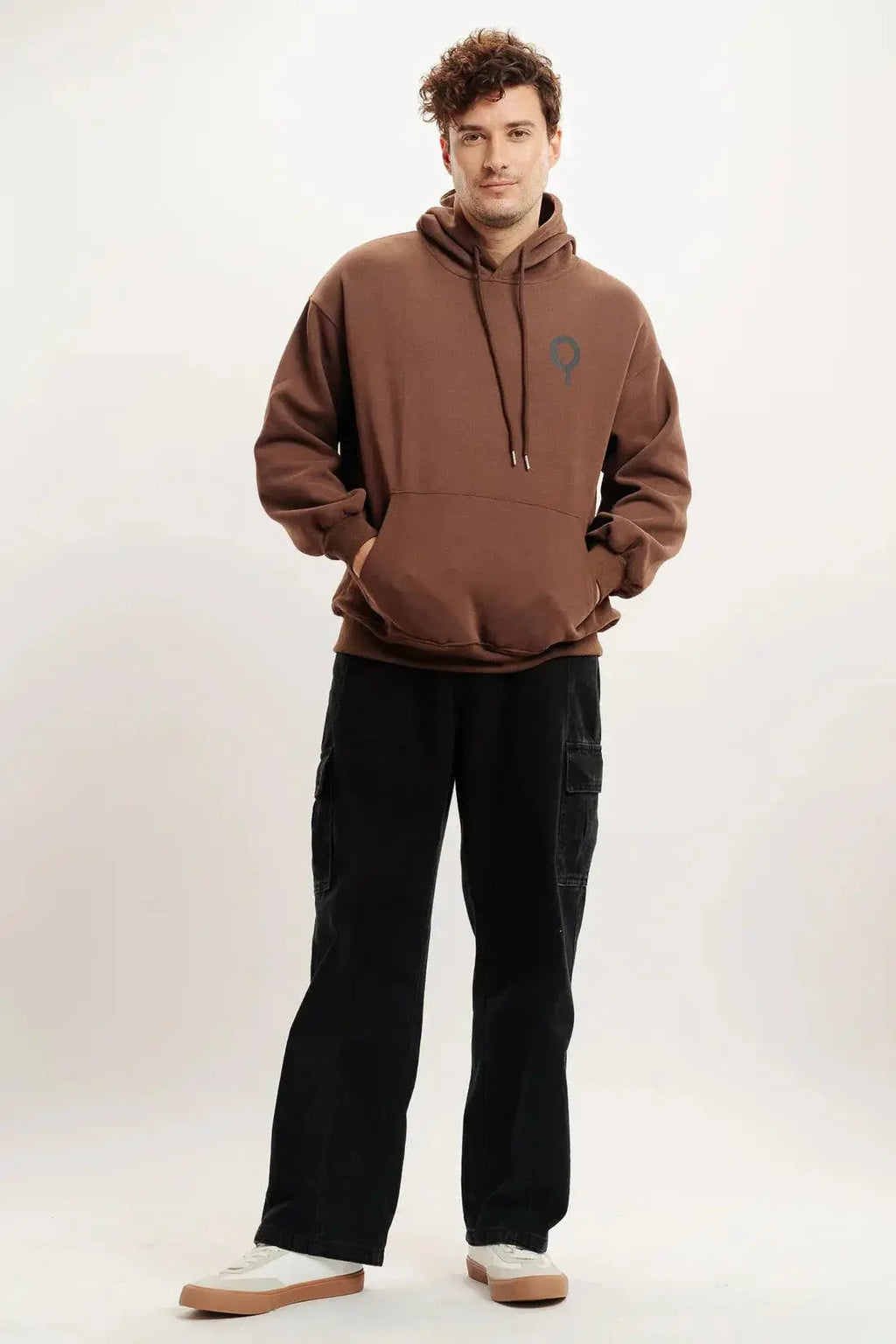 Man modeling brown oversized hoodie with logo, black cargo pants, and white sneakers