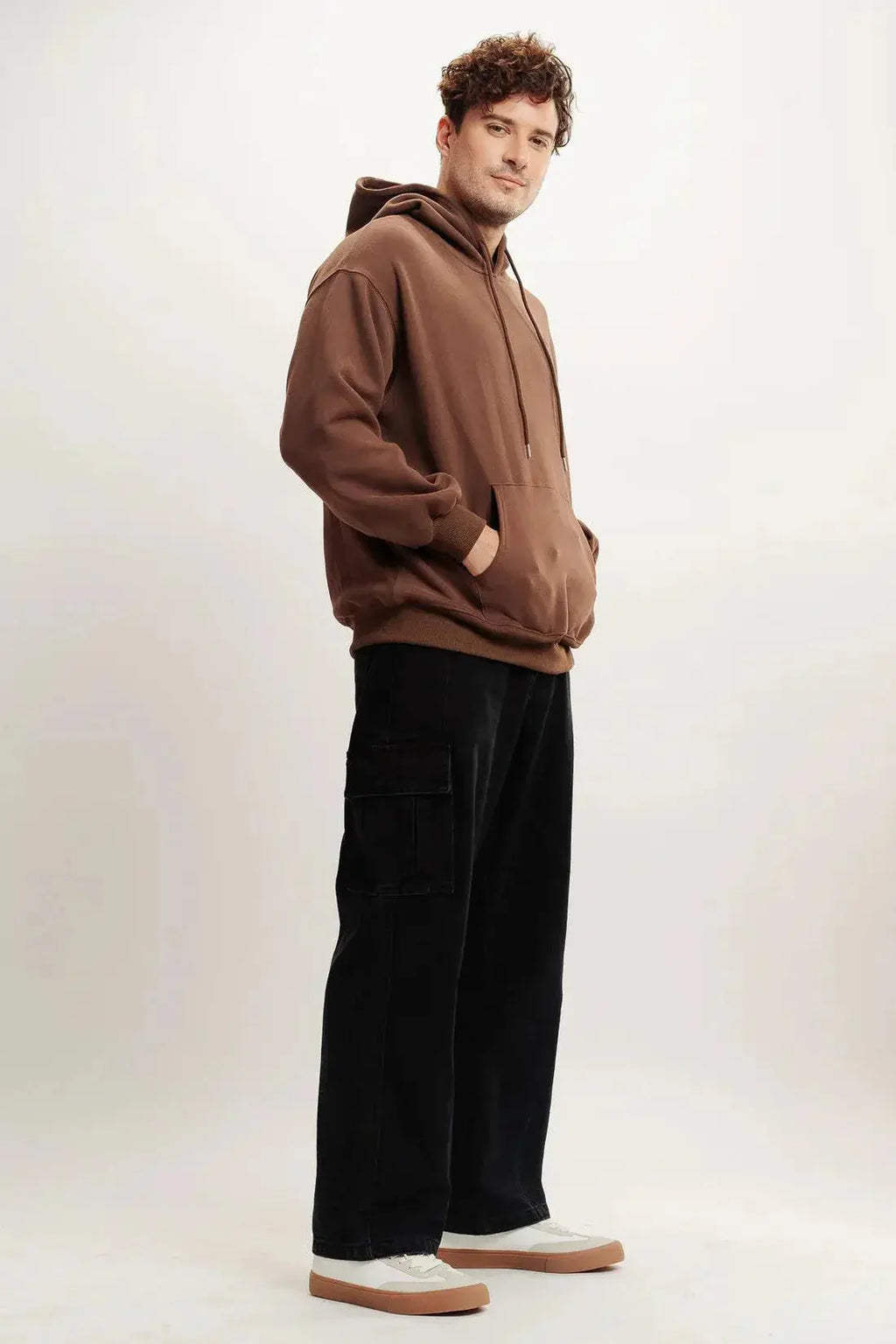 Man modeling brown streetwear hoodie with black cargo pants and white sneakers