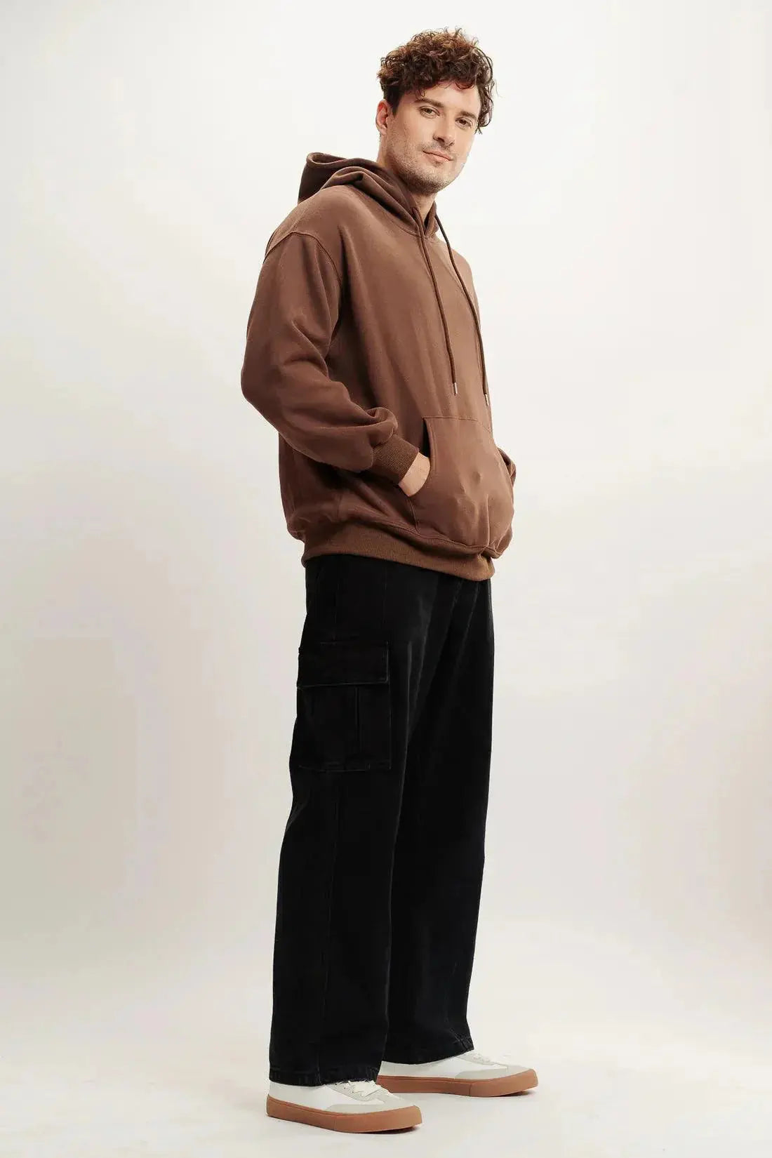 Man modeling brown streetwear hoodie with black cargo pants and white sneakers