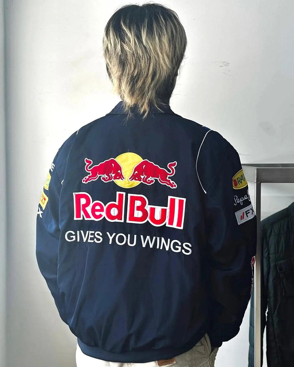Man wearing navy Red Bull racing jacket with bold back logo and patch details, streetwear style