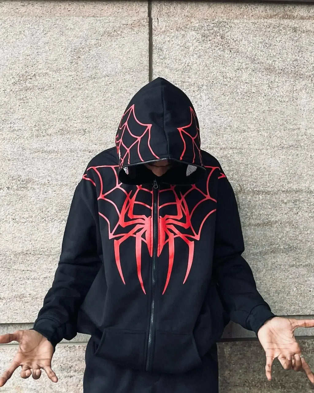 Man wearing black zip-up hoodie with red spider web and spider graphic, urban streetwear style