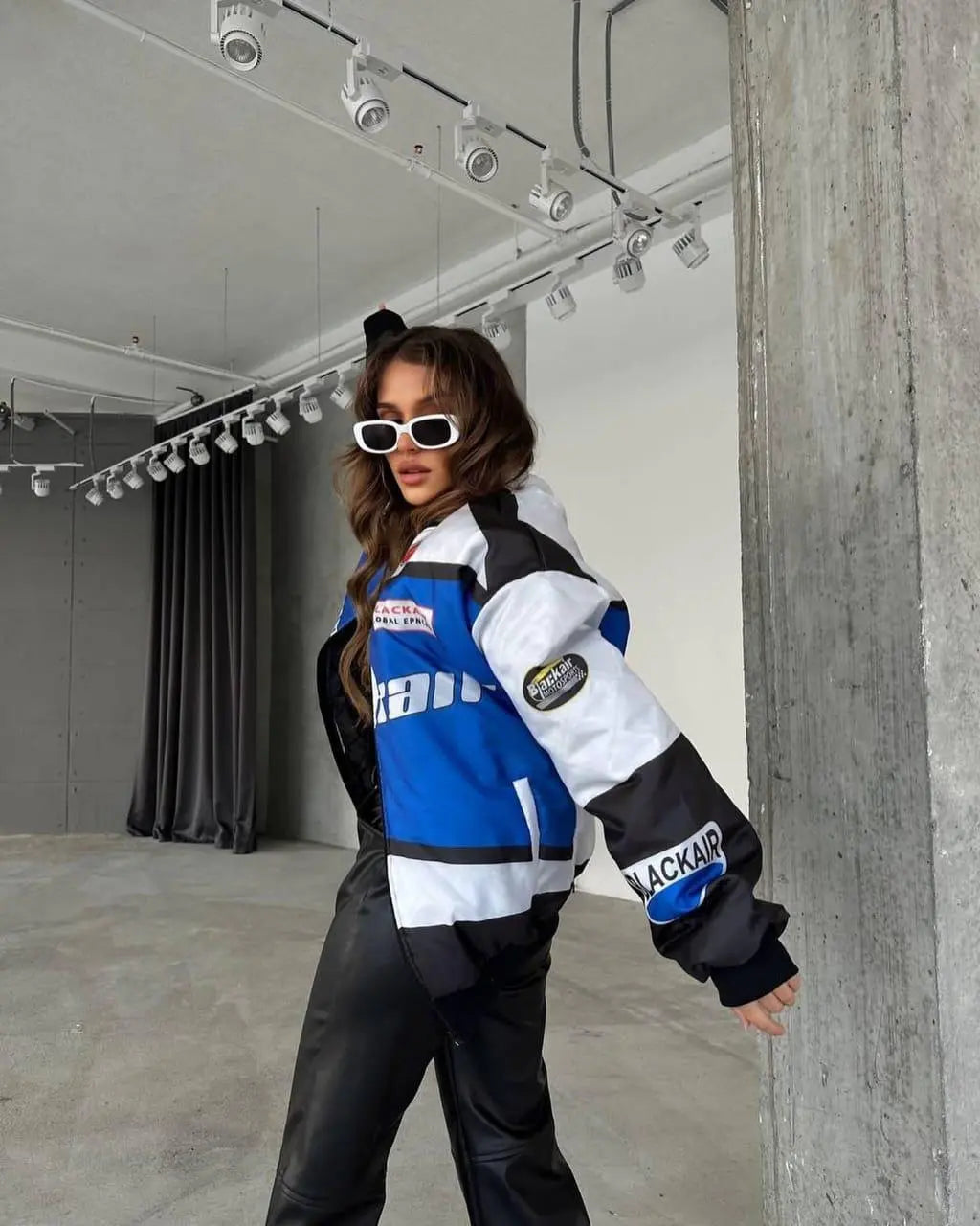 Woman wearing a blue and white colorblock streetwear jacket and black pants in a modern loft