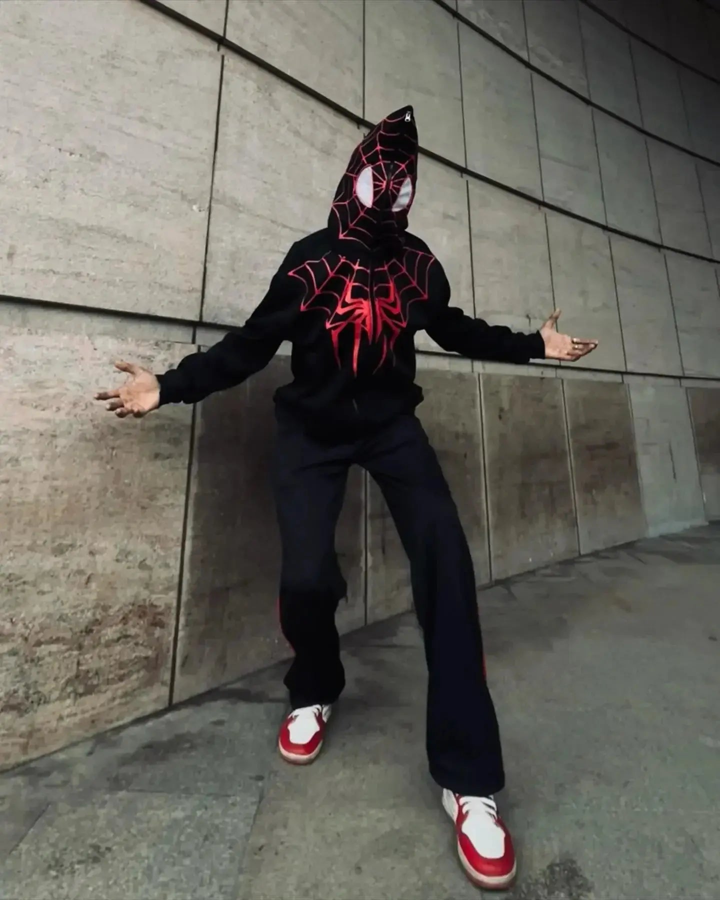 Person wearing black and red Spider-Man zip-up hoodie with mask, streetwear style, urban setting