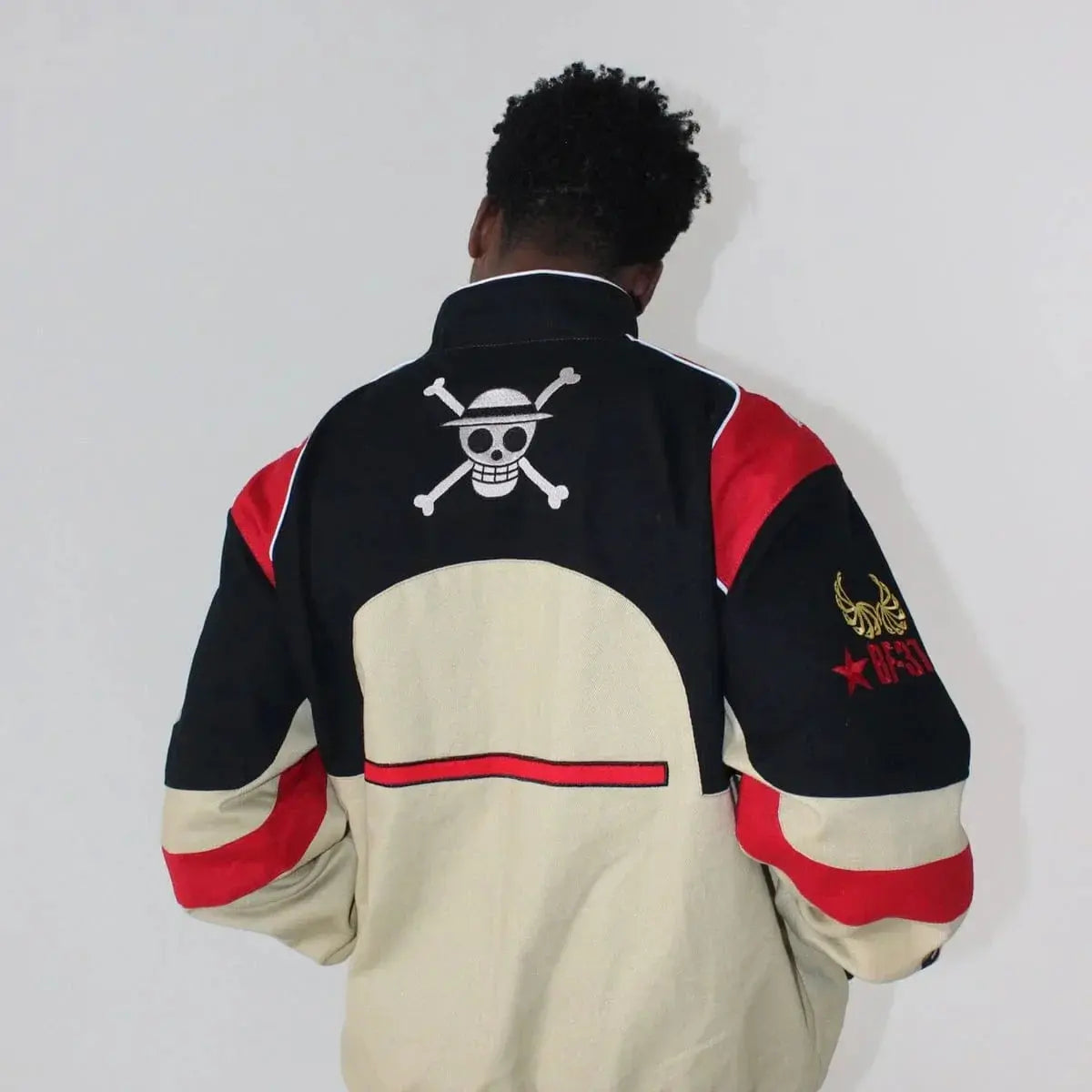 Man wearing black, beige, and red varsity jacket with anime skull logo and embroidery on back.